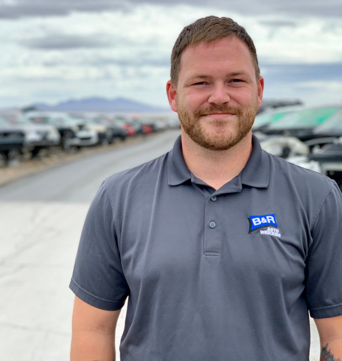 A technician in a grey polo shirt in front of a vehicle lot